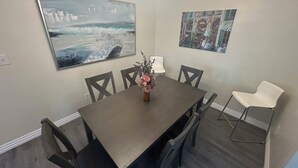 A dining area with a rectangular table, six chairs, a vase with flowers, and two wall-mounted artworks. - Enjoyable historic Duplex next door to Hutchins BBQ (McKinney)