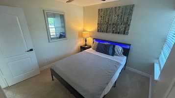 Quarto com cama, ventilador de teto, mesa de cabeceira com abajur, espelho e um quadro na parede.