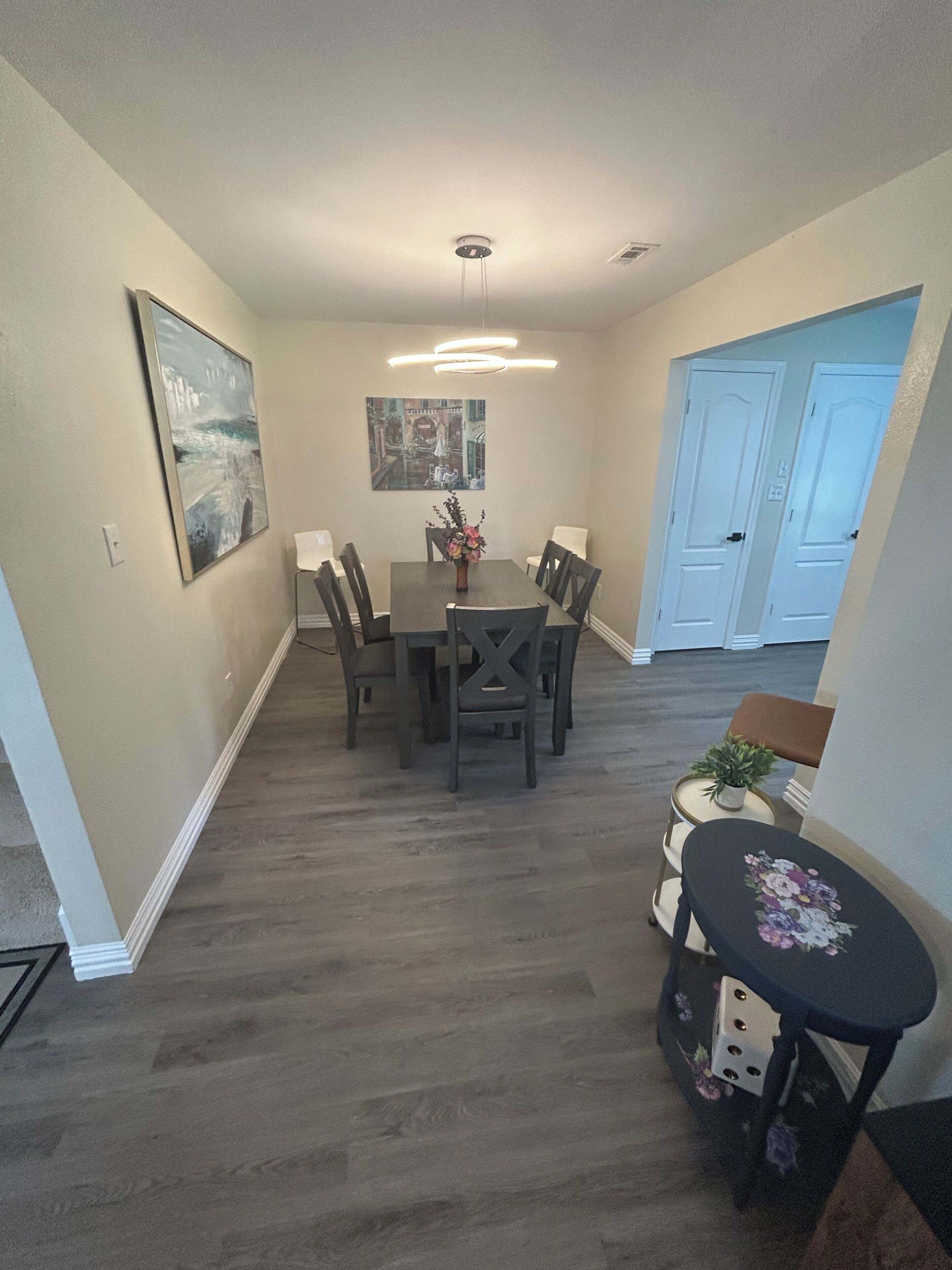 A dining area with a table and chairs, a ceiling light fixture, and a door in the background.