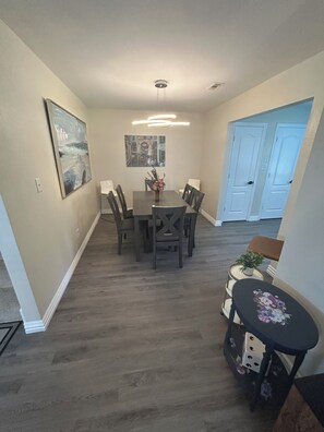 Un coin repas avec une table et des chaises, un luminaire au plafond et une porte visible au fond.
