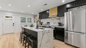 A modern kitchen with a marble island, stainless steel appliances, and black cabinetry. - Family-Friendly 4BR Home | Near Downtown ATL (Atlanta)