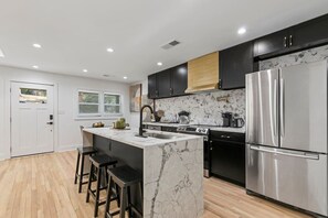 A modern kitchen with a marble island, stainless steel appliances, and black cabinetry. - Family-Friendly 4BR Home | Near Downtown ATL (Atlanta)