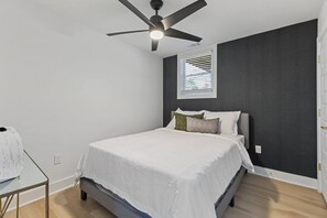 A bedroom with a bed, a ceiling fan, a window with blinds, and a small table with a lamp. - Family-Friendly 4BR Home | Near Downtown ATL (Atlanta)