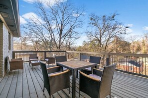 Una terraza con mobiliario de mimbre y una mesa, rodeada de árboles y un cielo despejado.