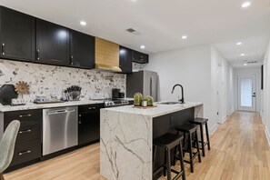 A modern kitchen with dark cabinets, a marble backsplash, stainless steel appliances, and a central island with stools. - Family-Friendly 4BR Home | Near Downtown ATL (Atlanta)