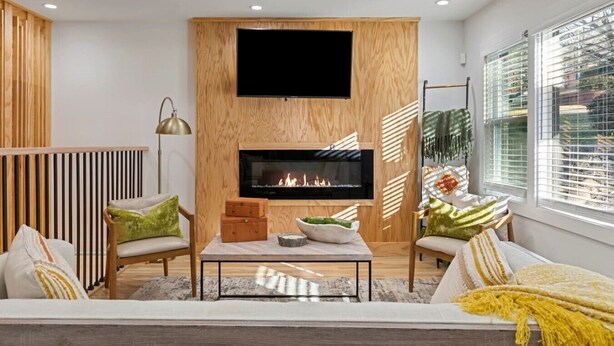 A modern living room with a fireplace, wooden paneling, and a large window with blinds. - Family-Friendly 4BR Home | Near Downtown ATL (Atlanta)