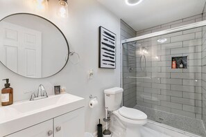 Ein modernes Badezimmer mit einem runden Spiegel, einer weißen Toilette und einer Duschkabine aus Glas.