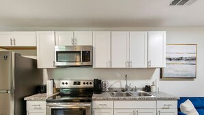 A compact kitchen with white cabinets, a stainless steel refrigerator, a microwave, an oven, and a sink. - Charming 2BR Rear Unit Retreat Near Atlanta (Lithia Springs)