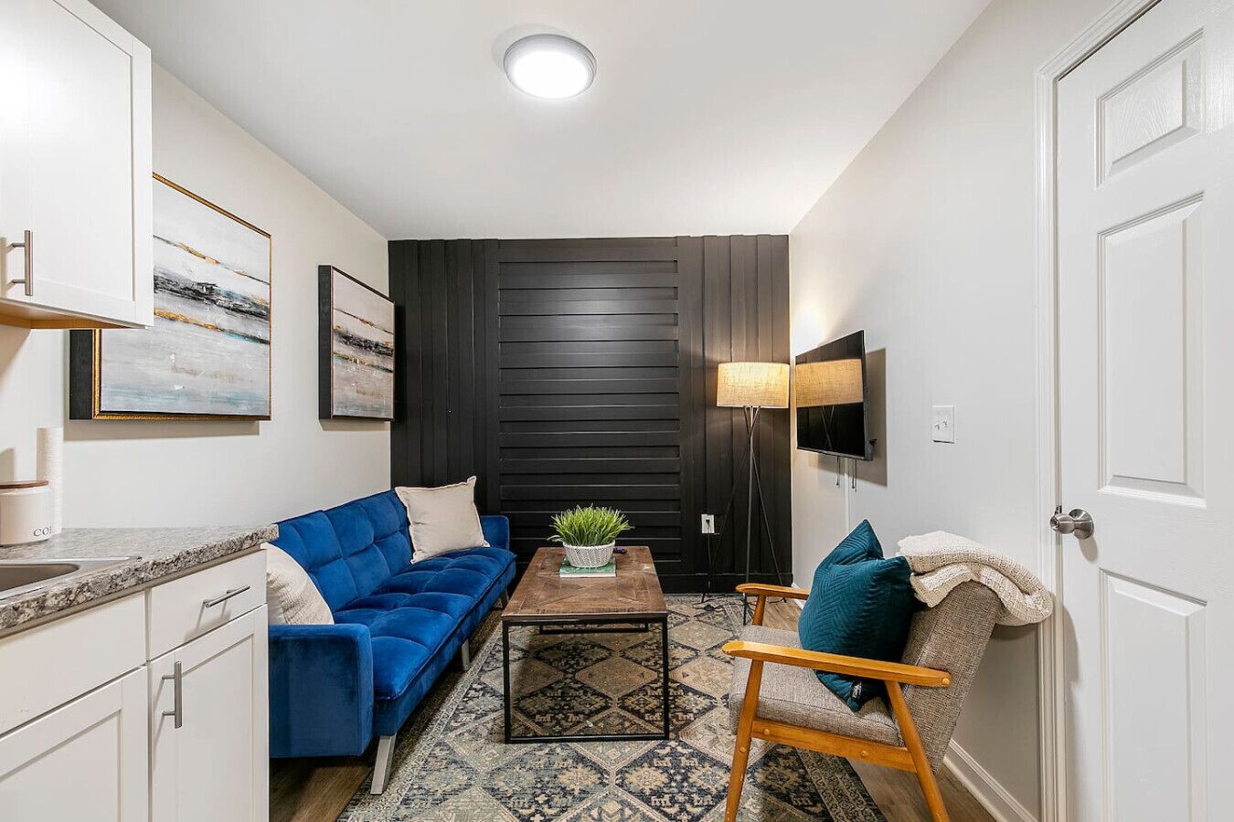 A compact living space with a sofa, armchair, coffee table, and a TV mounted on the wall.