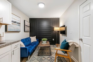 Ein gemütlicher Wohnbereich mit Sofa, Sessel, Couchtisch und einem an der Wand befestigten Fernseher.