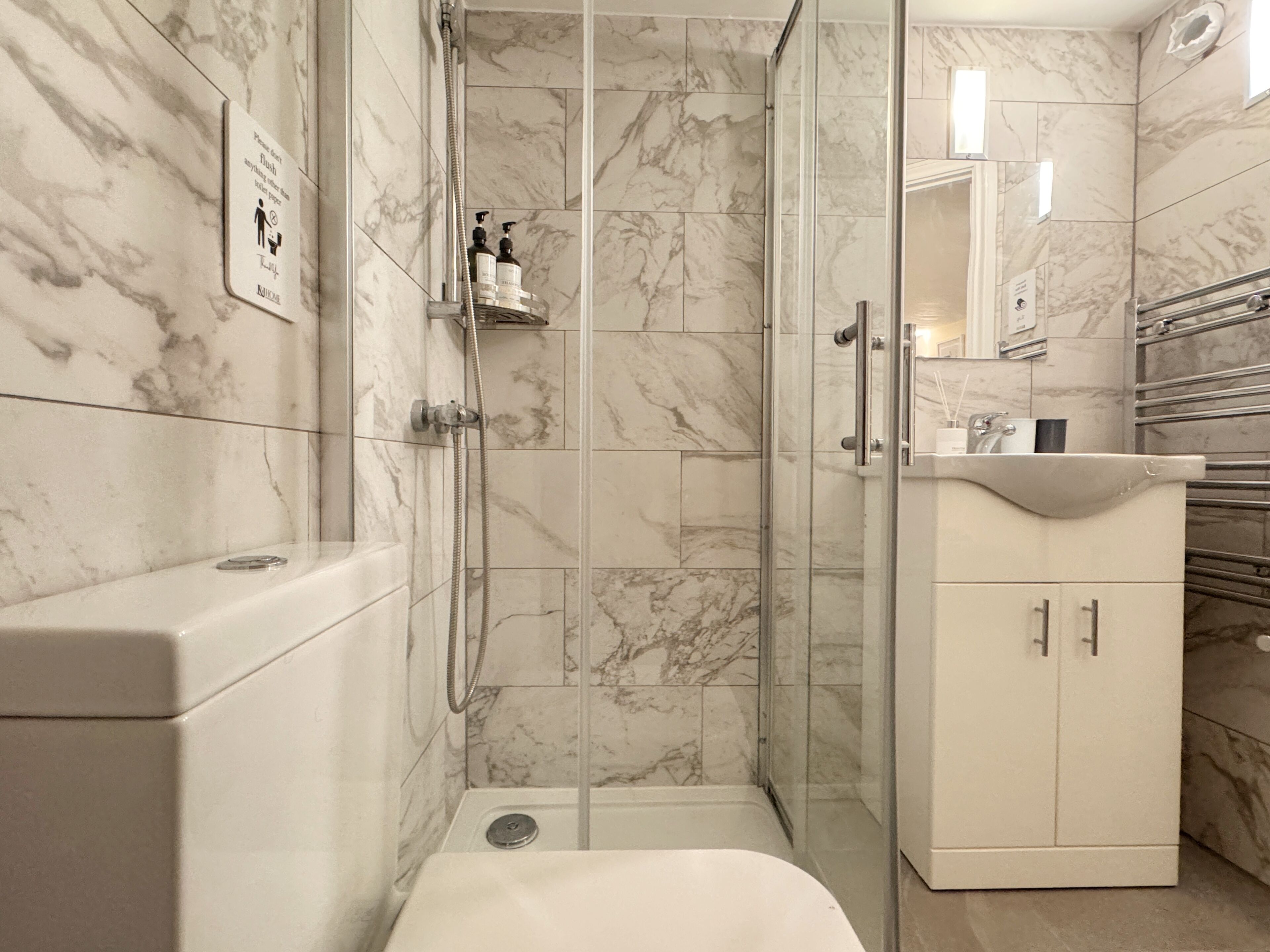 A bathroom with a glass-enclosed shower, a toilet, and a sink with a mirror above it.