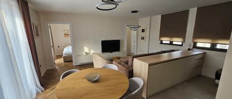 A modern kitchen with a dining area, a TV, and a large window.