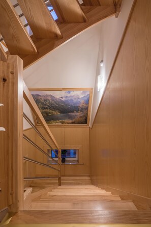 Eine hölzerne Treppe führt zu einem Schlafzimmer auf dem Dachboden, mit einem großen Fenster mit Blick auf eine gebirgige Landschaft.