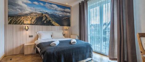 A hotel room with a bed, a view of mountains, a window with curtains, and a patterned rug.