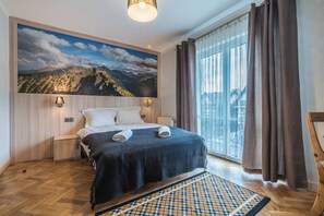 A hotel room with a bed, a view of mountains, a window with curtains, and a patterned rug. - Fantastic 9-bedroom house in Zakopane for your perfect getaway (Zakopane)