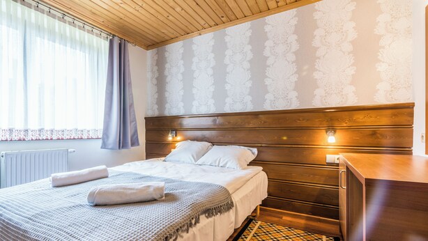 A neatly made bed with a patterned bedspread and two pillows, a wooden headboard, a bedside table with a lamp, and a patterned rug on the floor. - Fantastic 9-bedroom house in Zakopane for your perfect getaway (Zakopane)
