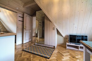 Ein Zimmer mit Holzwänden, einem Fischgrätparkett, einem Fernseher und einer Tür zu einem anderen Raum.