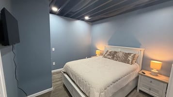 A bedroom with a bed, nightstands, a lamp, and a TV mounted on the wall.