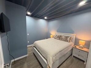 Een slaapkamer met een bed, nachtkastjes, een lamp en een televisie aan de muur.