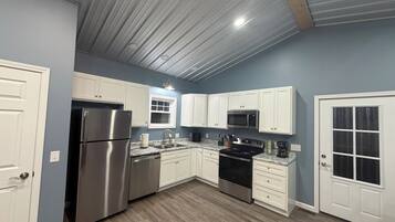 A modern kitchen with white cabinets, stainless steel appliances, and a wooden floor.