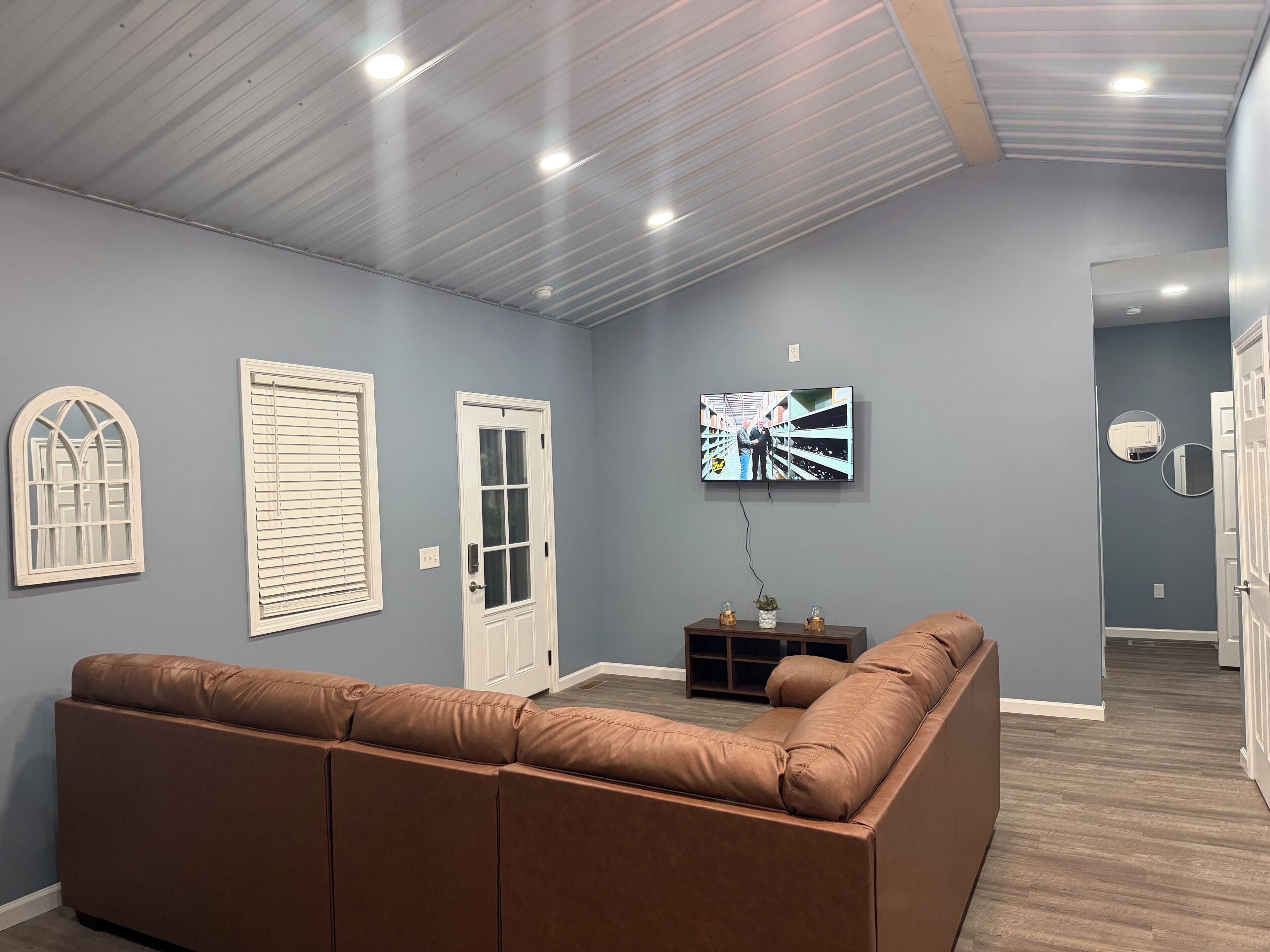 A living room with a brown leather sofa, a television mounted on the wall, and a door with a window.