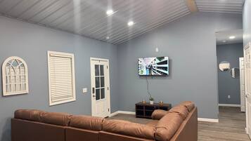 A living room with a brown leather sofa, a television mounted on the wall, and a door with a window.