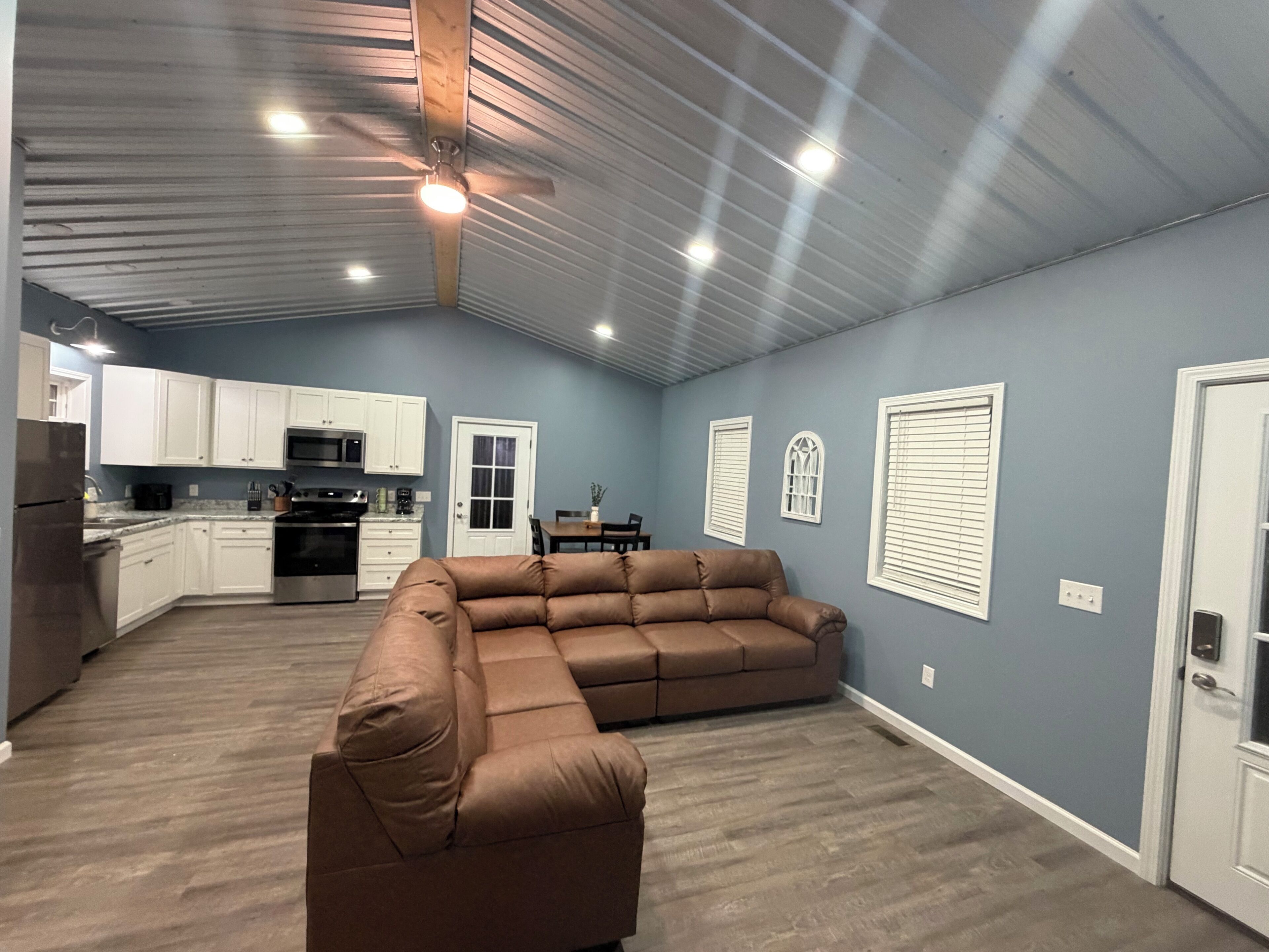 A spacious living area with a sectional sofa, a dining table with chairs, and a kitchen area with white cabinets and appliances.