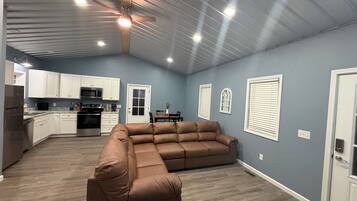 A spacious living area with a sectional sofa, a dining table with chairs, and a kitchen area with white cabinets and appliances.