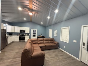 A spacious living area with a sectional sofa, a dining table with chairs, and a kitchen area with white cabinets and appliances. - Cute and Convenient Cabin located close to Dale Hollow Lake-Cabin#4 (Burkesville)