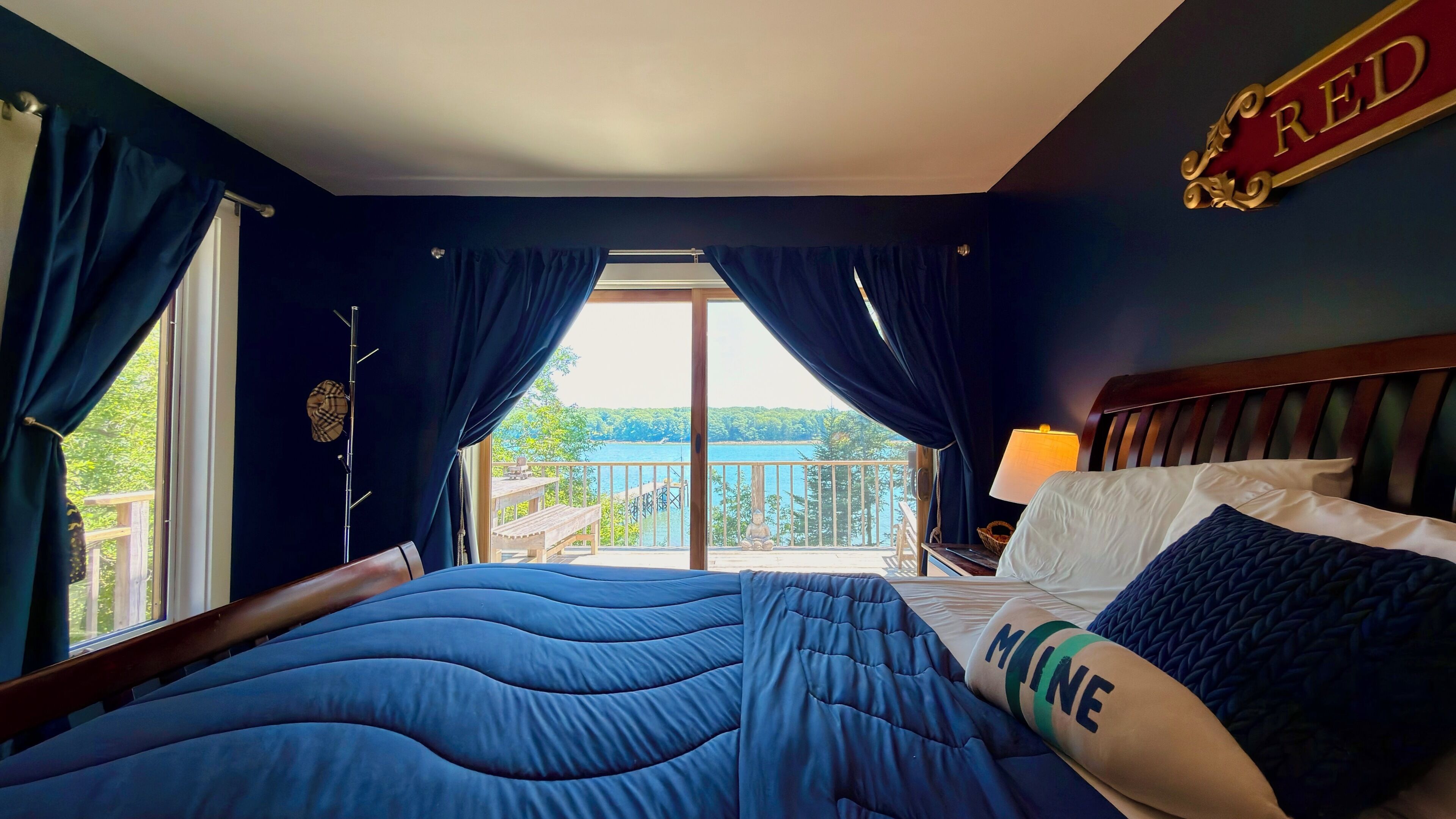 A bedroom with a bed, curtains, a view of the outdoors, a lamp, and a sign with the word 'RED'.
