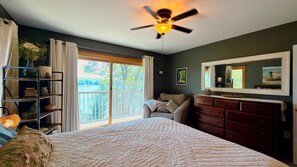 A bedroom with a bed, a dresser, a mirror, a ceiling fan, and a view of a balcony. - Arden House | A Riverside Vacation Rental in Midcoast Maine (Cushing)