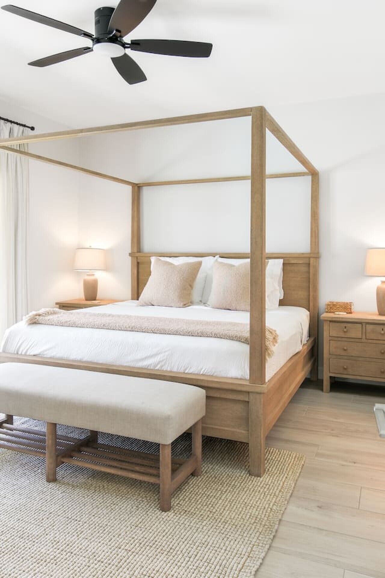 Una cama con dosel de madera, un banco al pie y un ventilador de techo.