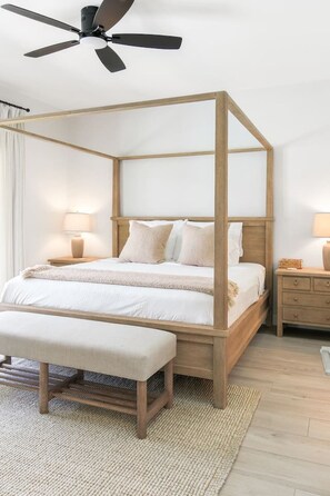 Un lit à baldaquin avec un cadre en bois, un banc au pied du lit et un ventilateur de plafond.