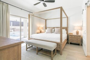 A bedroom with a four-poster bed, a bedside table, a bench, and a view of a swimming pool. - Mohican Escape | Stylish Backyard Retreat (Lake Havasu City)