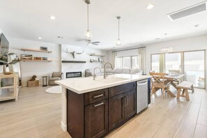 A modern kitchen with a central island, dark cabinetry, and a dining area with a wooden table and chairs. - Mohican Escape | Stylish Backyard Retreat (Lake Havasu City)