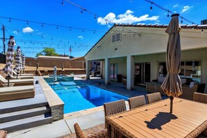 Ein Schwimmbecken mit Liegestühlen und Sonnenschirmen, eine überdachte Terrasse und Lichterketten.