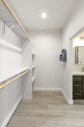 A walk-in closet with open shelving, a mirrored closet door, and a light-colored wooden floor. - Mohican Escape | Stylish Backyard Retreat (Lake Havasu City)