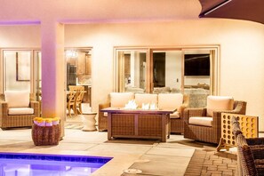 A poolside area with wicker furniture, a fire feature, and a view of the interior. - Mohican Escape | Stylish Backyard Retreat (Lake Havasu City)