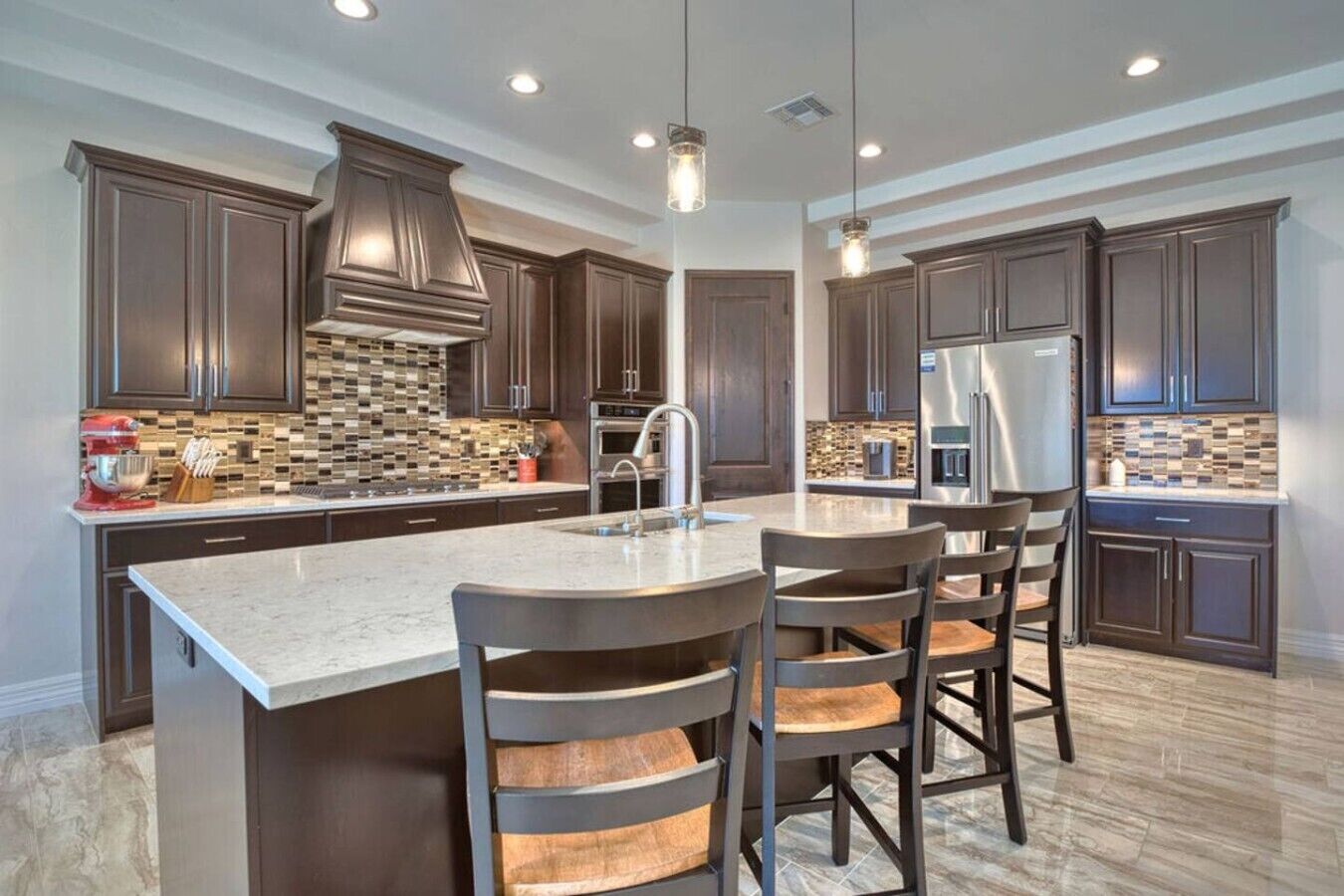 A modern kitchen with dark wood cabinets, a large island with bar stools, stainless steel appliances, and pendant lighting.