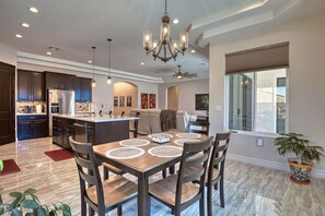 A modern kitchen with dark cabinetry, a central island, and a dining area with a wooden table and chairs. - Luxury Retreat | Hot Tub | RV Garage | EV Charger (Lake Havasu City)