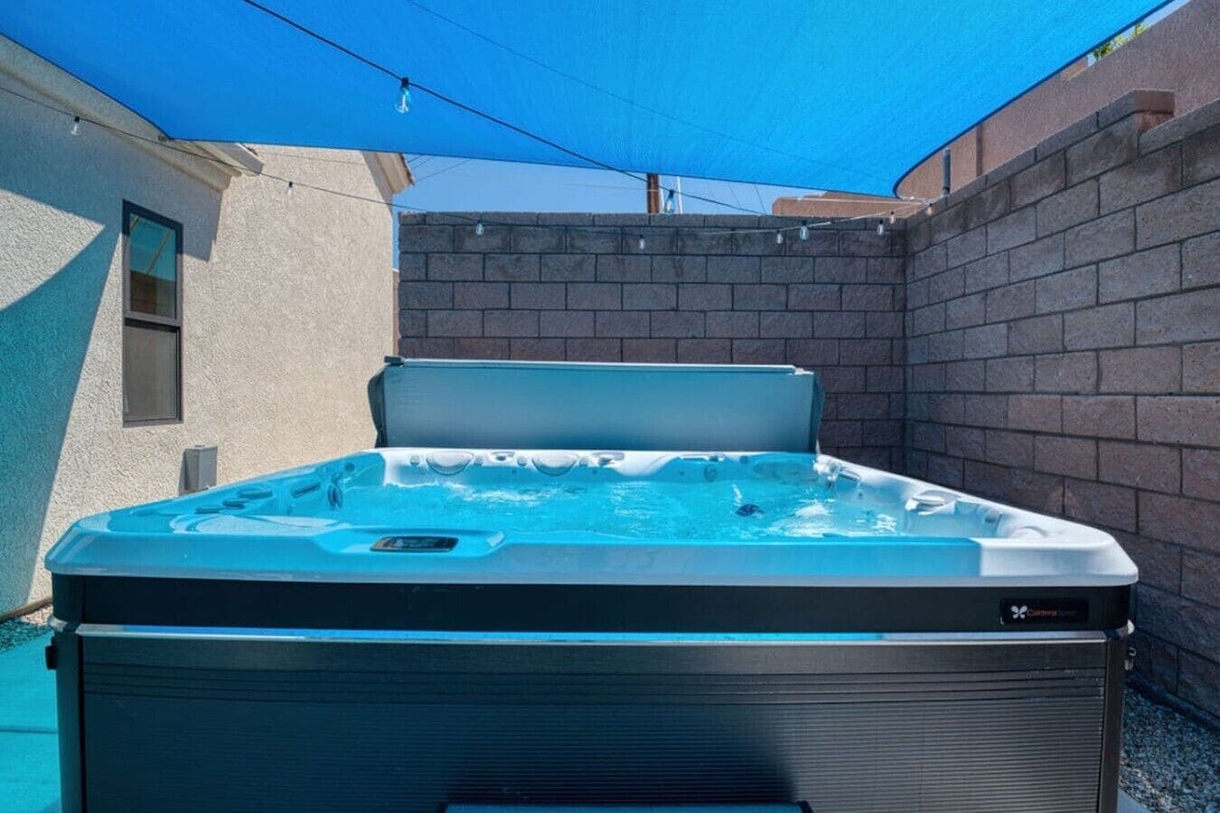 Un jacuzzi con tapa, rodeado por un muro de ladrillo y un toldo azul.