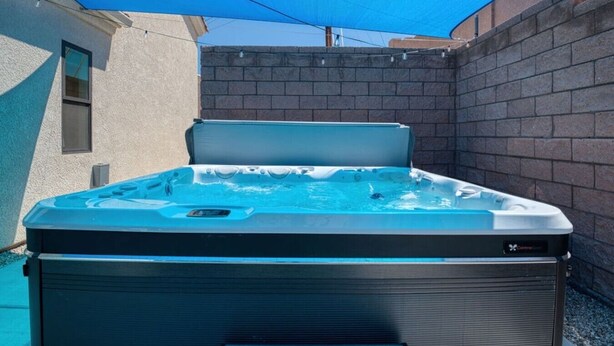 Ein Whirlpool mit Abdeckung, umgeben von einer Ziegelmauer und einem blauen Sonnensegel.