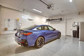 A blue BMW M50 in a clean, well-lit garage with a white door, a white ceiling, and a projector mounted on the ceiling. - Luxury Retreat | Hot Tub | RV Garage | EV Charger (Lake Havasu City)