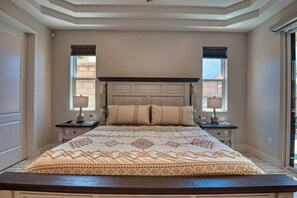 A bedroom with a large bed, two bedside tables with lamps, a decorative headboard, and windows with blinds. - Luxury Retreat | Hot Tub | RV Garage | EV Charger (Lake Havasu City)