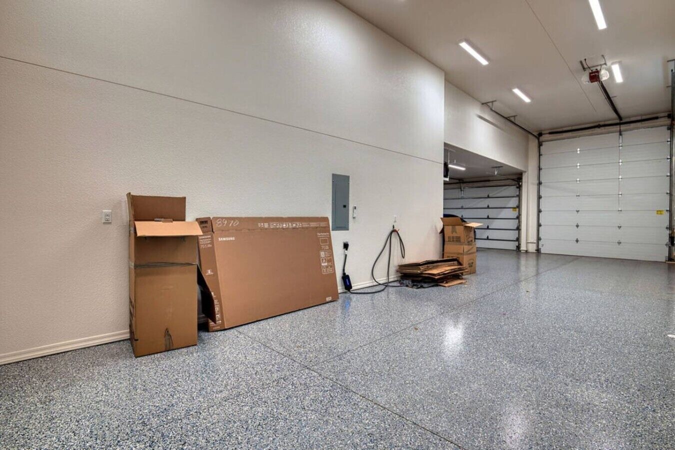 A spacious indoor area with a tiled floor, a closed garage door, and cardboard boxes against the wall.
