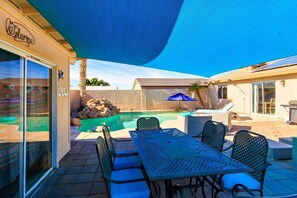 Un espace piscine avec une table et des chaises, un patio couvert et un bâtiment sur lequel est affiché un panneau « Bienvenue ».