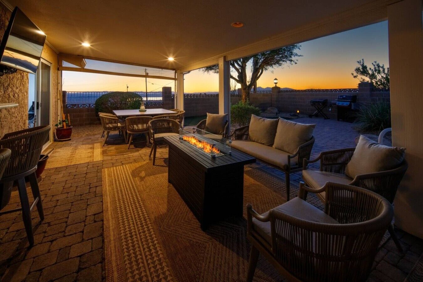An outdoor patio with a fire feature, seating, and a view of the sunset.