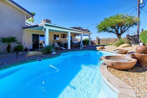 Ein Schwimmbecken mit überdachter Terrasse, einem kleinen Wasserfall und einem angelegten Garten mit Steinen und Pflanzen.