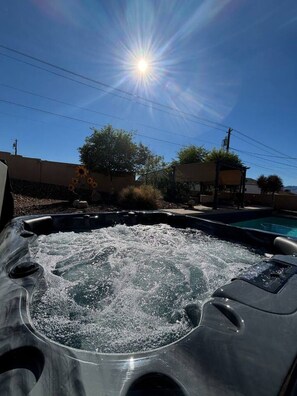 Een jacuzzi met waterstralen, omringd door een zwembad, onder een heldere lucht.