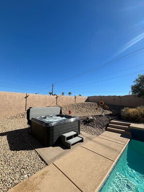 A hot tub with steps leading to a pool, surrounded by a landscaped area with rocks and plants. - Sleeps 12 w/ ping pong & pool table| comfort + (Lake Havasu City)